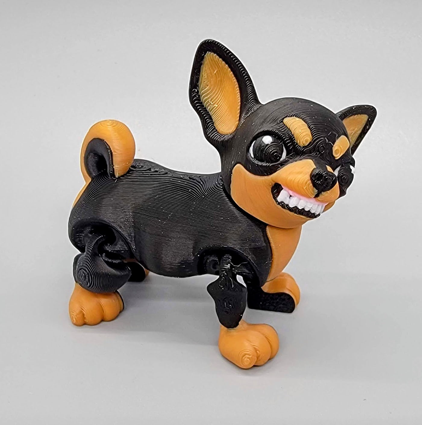 3D printed articulated Chihuahua toy in black and tan with cartoon-style crazy teeth expression – poseable dog figure with bold facial features.