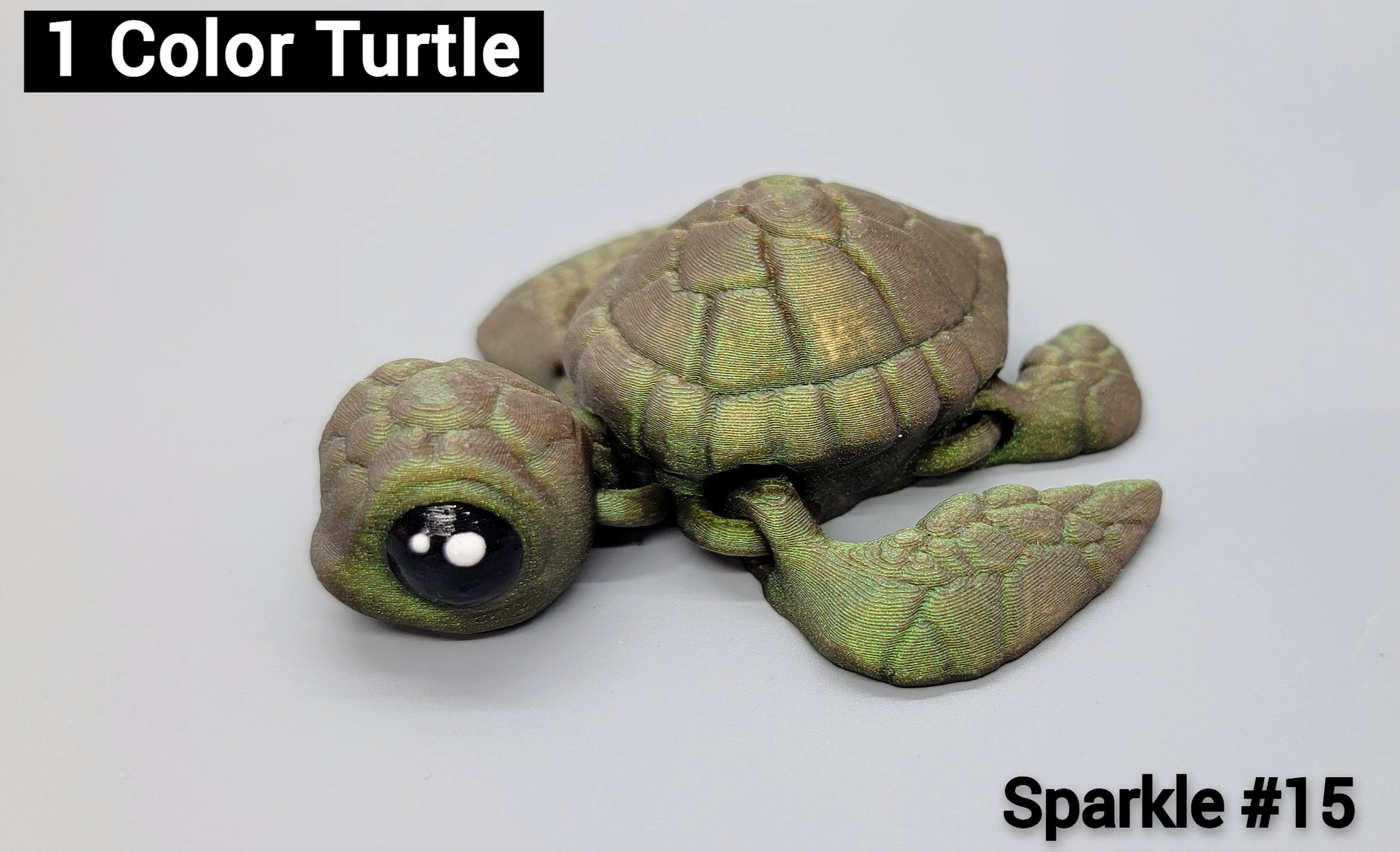 3D printed baby sea turtle toy in Sparkle #15 filament – a shimmery green and brown articulated design with big black cartoon eyes.