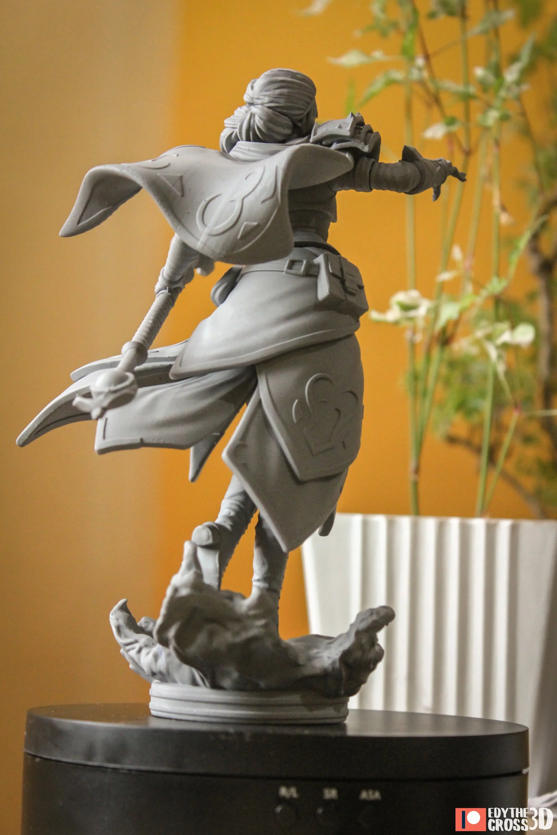Gray statue of a character on a black pedestal against a yellow wall with a plant.