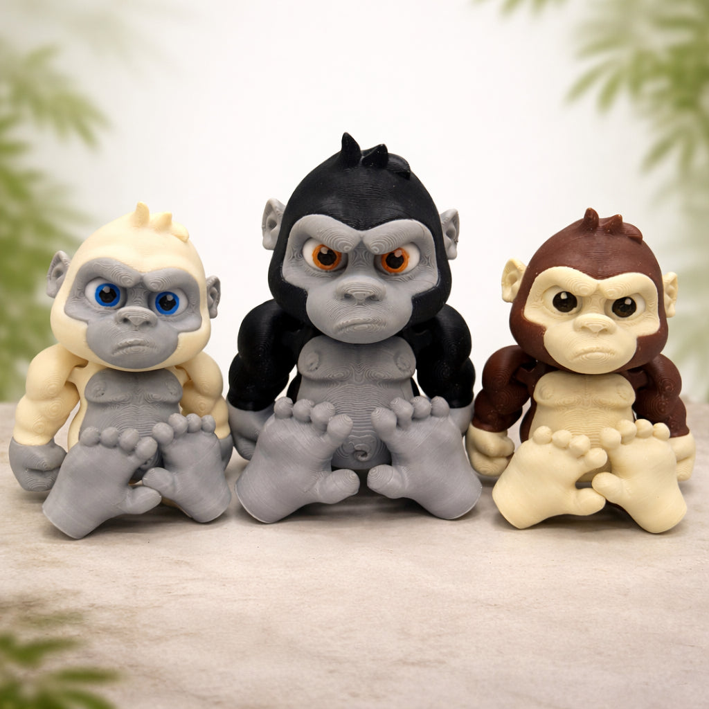 Articulated baby gorilla toy featuring three cute 3D printed chibi gorilla figures in black gray and brown with oversized heads expressive eyes and movable limbs displayed on a neutral studio background with subtle nature accents for play display or gifts