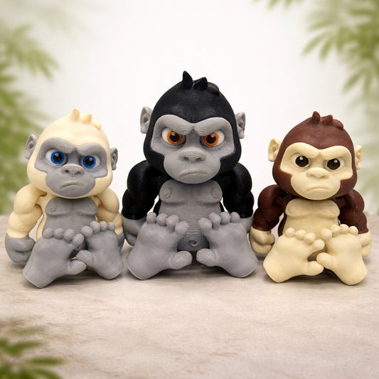 Articulated baby gorilla toy featuring three cute 3D printed chibi gorilla figures in black gray and brown with oversized heads expressive eyes and movable limbs displayed on a neutral studio background with subtle nature accents for play display or gifts