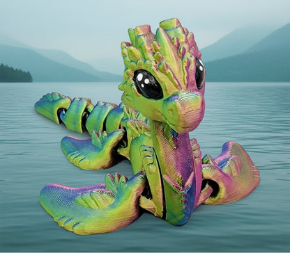 Articulated baby Nessie toy in rainbow colors sitting in water with mountains in the background, flexible 3D printed Loch Ness style creature toy and collectible