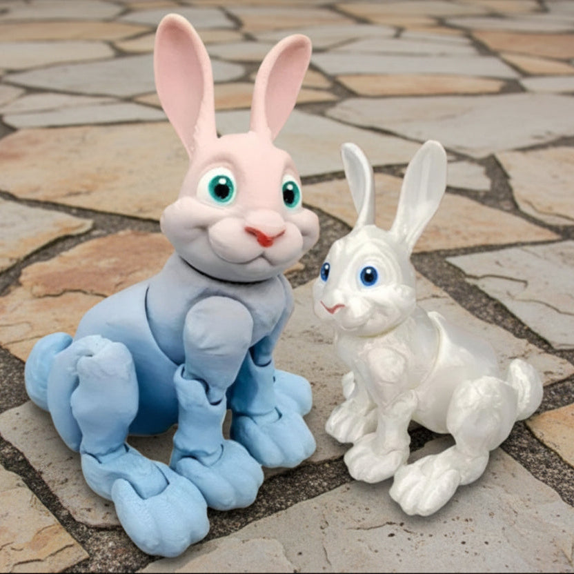 Two smiling sitting rabbits, one gradient blue and pink, one white on a stone surface