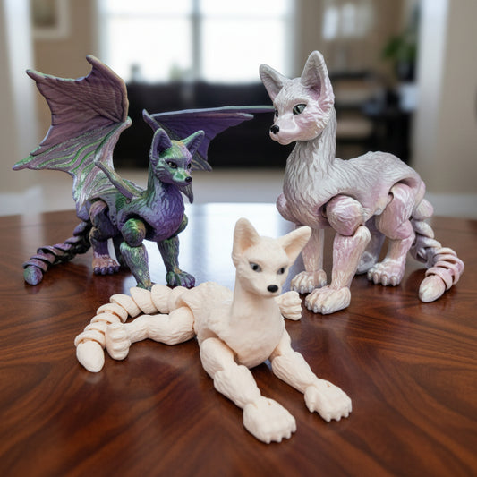 Articulated cat dragon toy displayed on a wooden table, shown in pastel lavender, mint green, deep purple, and cream white colorways. Features short hair and long hair variants with optional wings or wingless designs, fully posable body, and customizable color options.