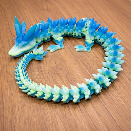 Articulated crystal dragon toy with translucent blue and green segments posed in a circular shape on a wooden surface