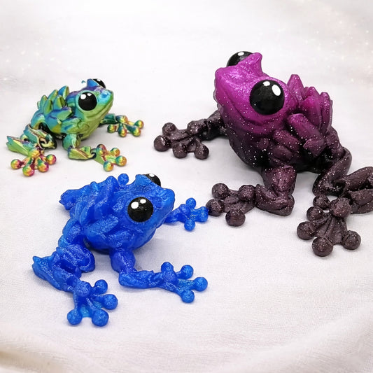 Three gemstone themed frogs in rainbow, sparkle gradient purple, and bright blue on a neutral background 