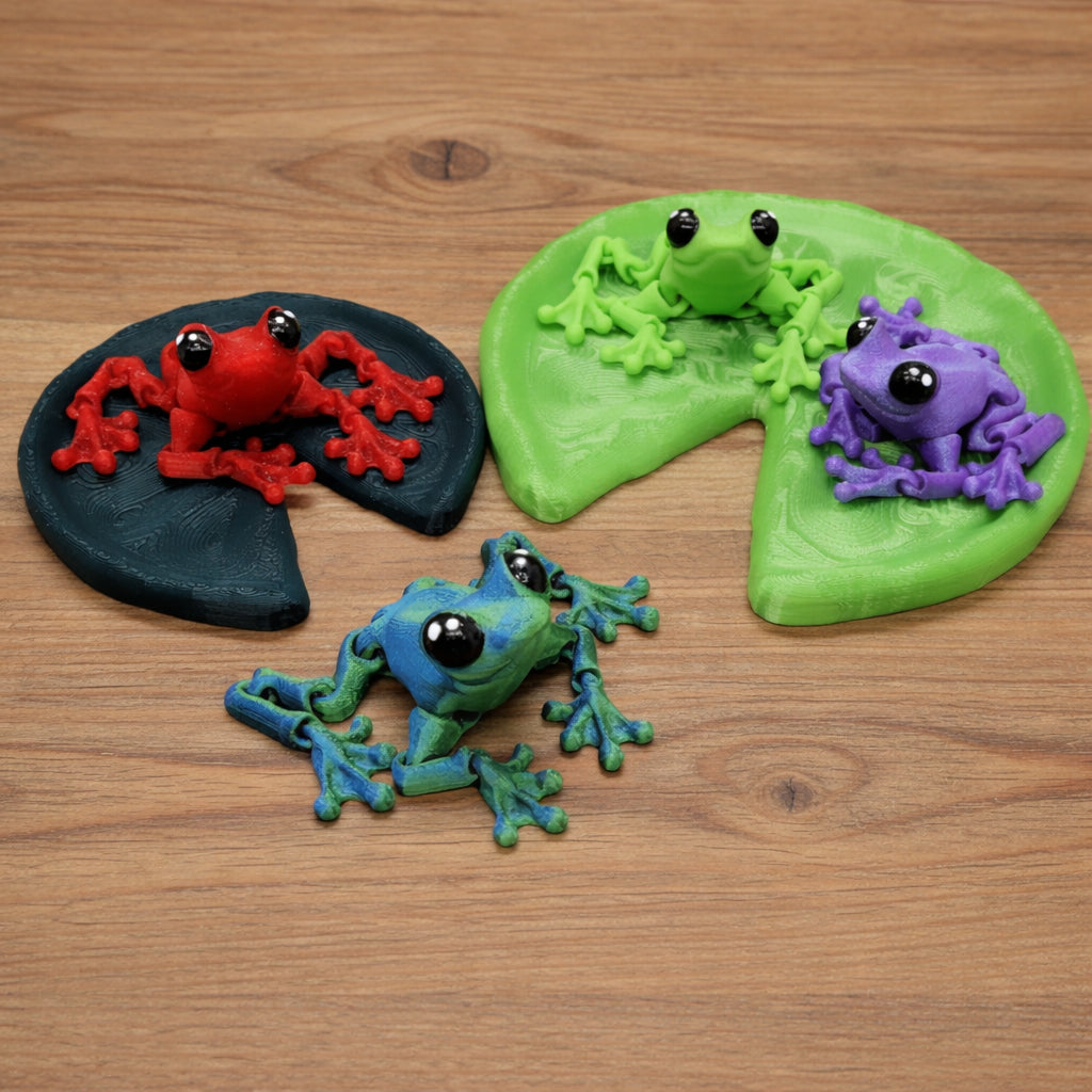 Articulated Tiny Cinder Frog toy in red, green, purple and blue on lily pads, 3D printed flexible frog figurines with glossy black eyes