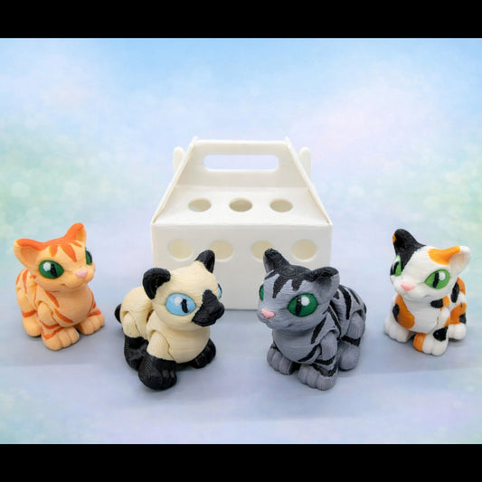Four small cat hatchling figures in different colors arranged in front of a white carry style container on a soft pastel background