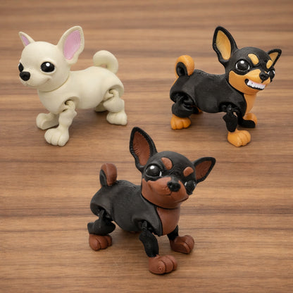 Three chibi-style articulated chihuahua dog toys in cream, black and tan, and dark brown color variants, featuring oversized ears, expressive eyes, and poseable legs, displayed on a warm wooden tabletop with a soft indoor background.