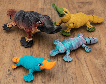 Custom articulated platypus toy set displayed on a brown surface, featuring four flexible 3D printed platypus figures in different colors and finishes with jointed bodies and textured details.