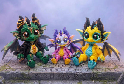 Three chibi dragon dolls on a stone platform: a large green Wizard Dragon with gold rings, a small pink and purple dragon, and a large yellow and turquoise dragon.⠋
