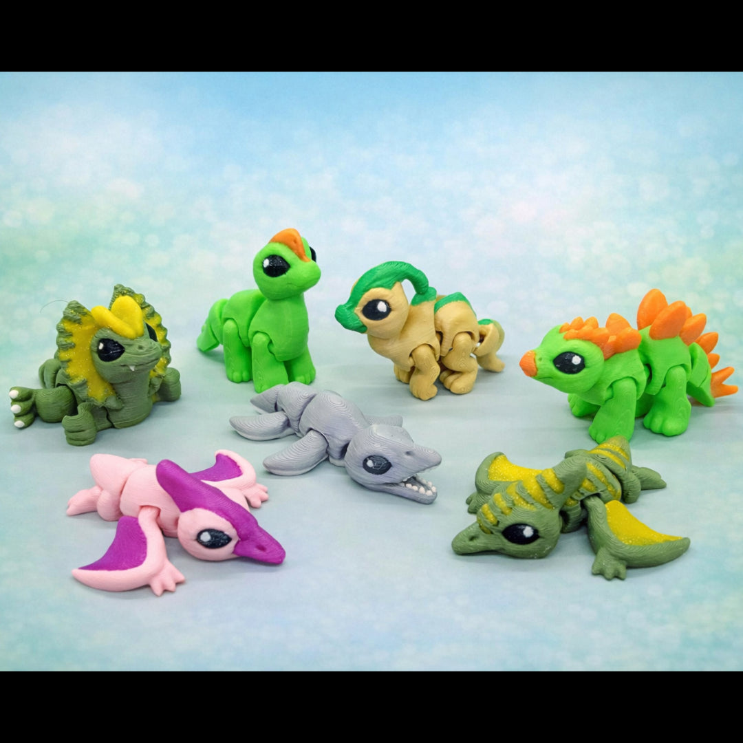 Colorful articulated dinosaur hatchling toys arranged in a circle on a soft blue background, featuring baby dinos in green, pink, gray, and yellow with different species and poses.
