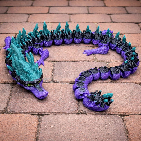Articulated Dragonfruit Dragon fidget toy in purple, black, and teal colors with a long flexible segmented body displayed on a brick patio background