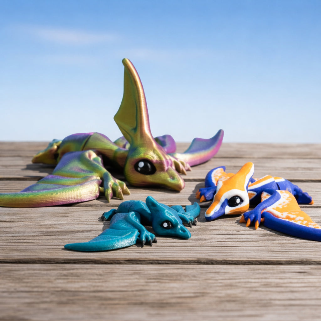 Articulated flappy pterodactyl and nyctosaurus toys in colorful finishes displayed on a wooden surface under a blue sky.