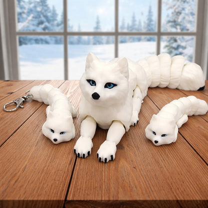 Flexi arctic fox toy or keychain featuring white articulated 3D printed fox figures with blue eyes and flexible segmented bodies shown on a brown surface with a winter background including a keychain version for play gifts or accessories