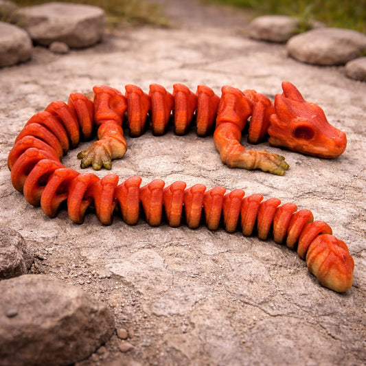 Red and orange articulated flexi skeleton dragon toy with a segmented spine, rib-like body sections, skull-style head, and clawed limbs, posed in an S shape on a textured stone ground with scattered rocks and a blurred outdoor background.