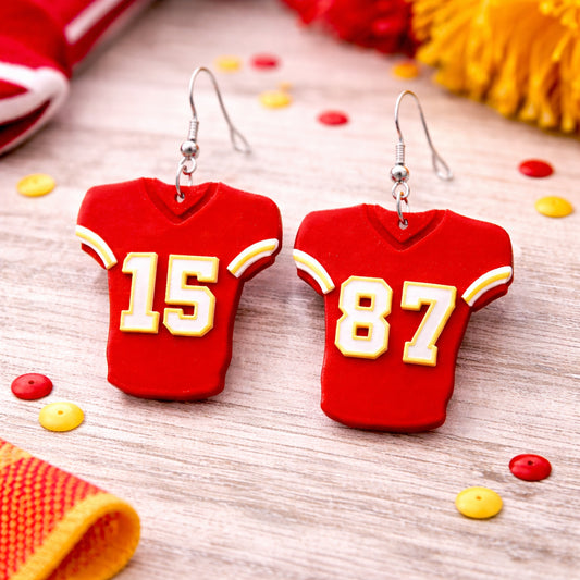 Red sports jersey earrings with numbers on a wooden surface.