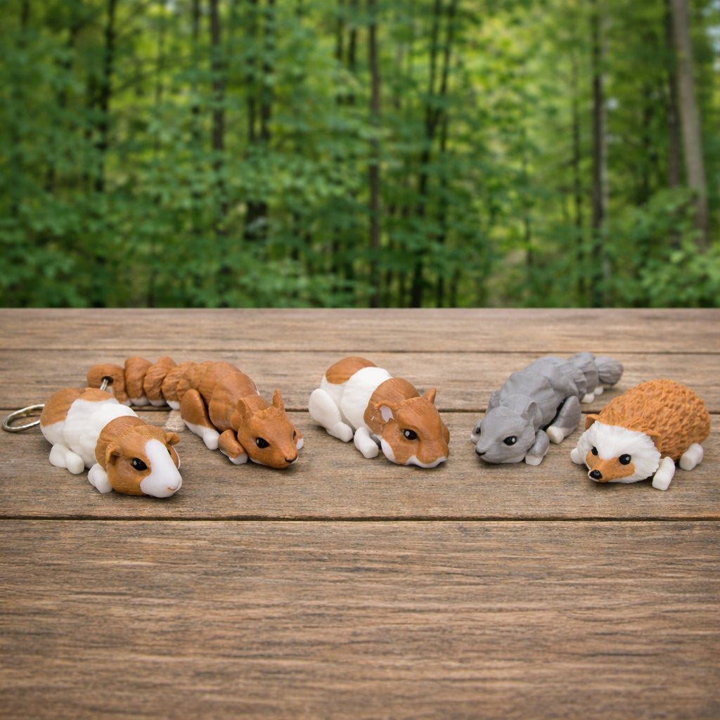 Set of five articulated mini animal toys on a wooden surface, including guinea pigs, a squirrel, and a hedgehog, shown outdoors with a blurred green forest background.