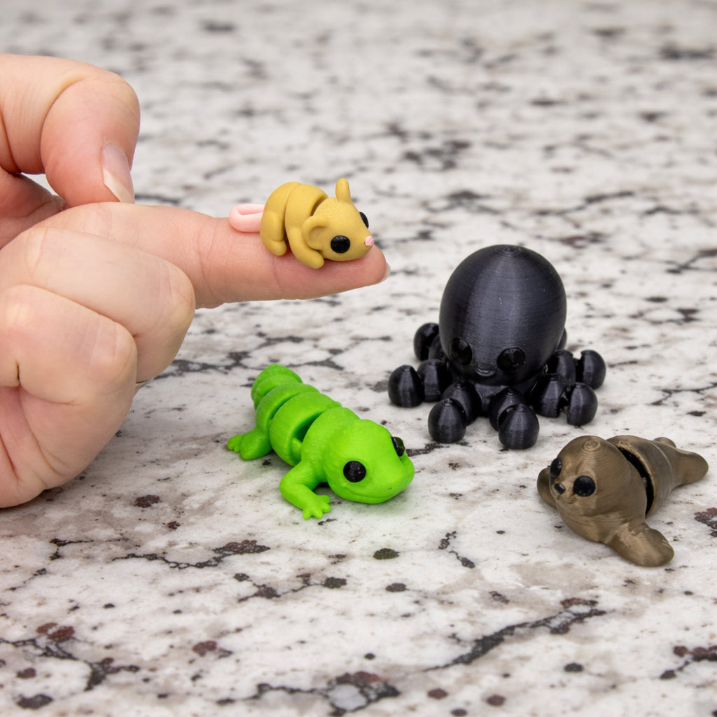 Mini micro fidget critters including a green articulated frog black octopus tan mouse and small brown creature shown on a stone countertop with a hand holding a tiny yellow mouse highlighting scale smooth 3D printed detail and sensory fidget play
