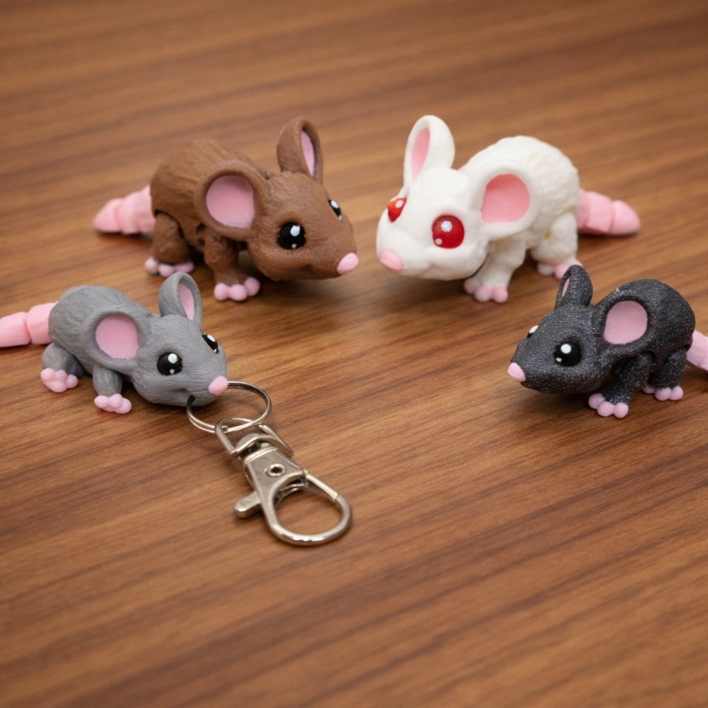 Articulated mini mouse toys and keychain in gray brown white and black with pink tails on a brown surface