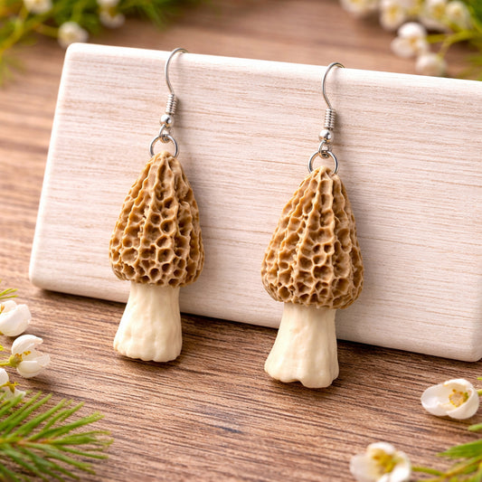 Pair of mushroom-shaped earrings on a wooden surface with a white card in the background.