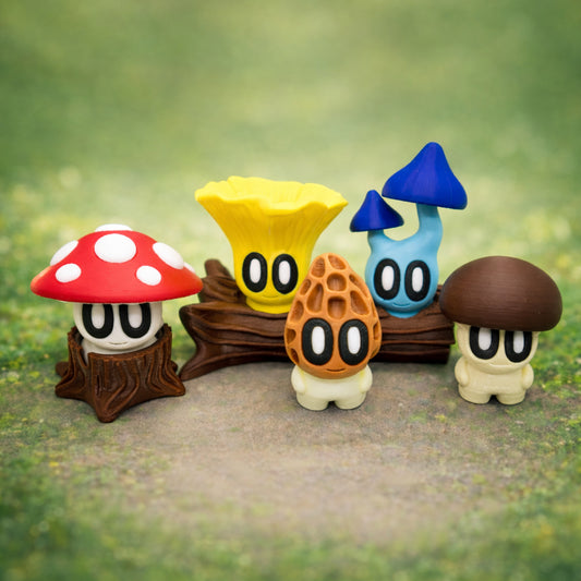 Five cute mushroom toy figures with cartoon eyes displayed on a mossy forest style background, featuring red, yellow, blue, and brown mushroom characters posed on a small log and stump.