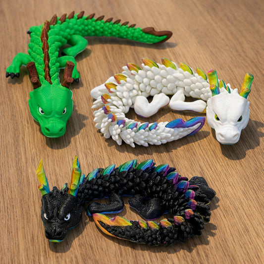 Articulated Noodle Dragon toy in green, white rainbow, and black rainbow color variants, featuring a flexible poseable body with detailed scales, displayed on a wooden tabletop