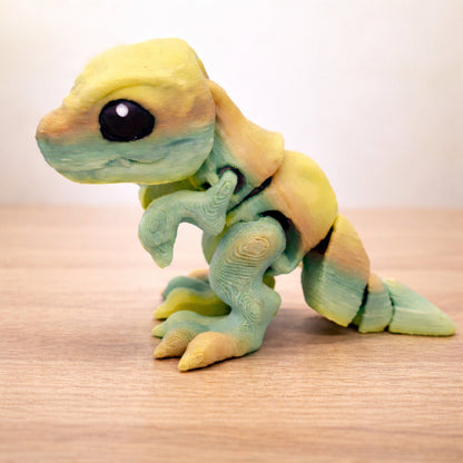 Articulated mini T rex toy in green gradient, standing on a light wooden table, ready to ship as a toy or keychain.