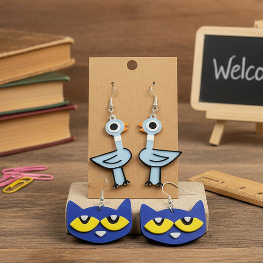 Great gifts for teachers that are light blue bird earrings and blue cat earrings being displayed on a teacher themed desk