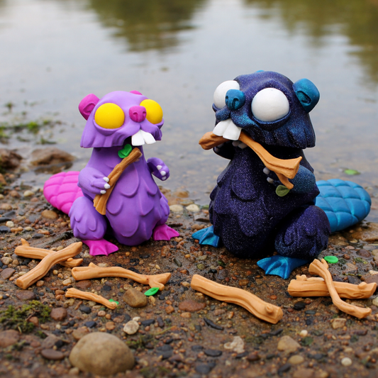 Two colorful articulated beaver toy figures with plastic branches on a rocky surface with water in the background