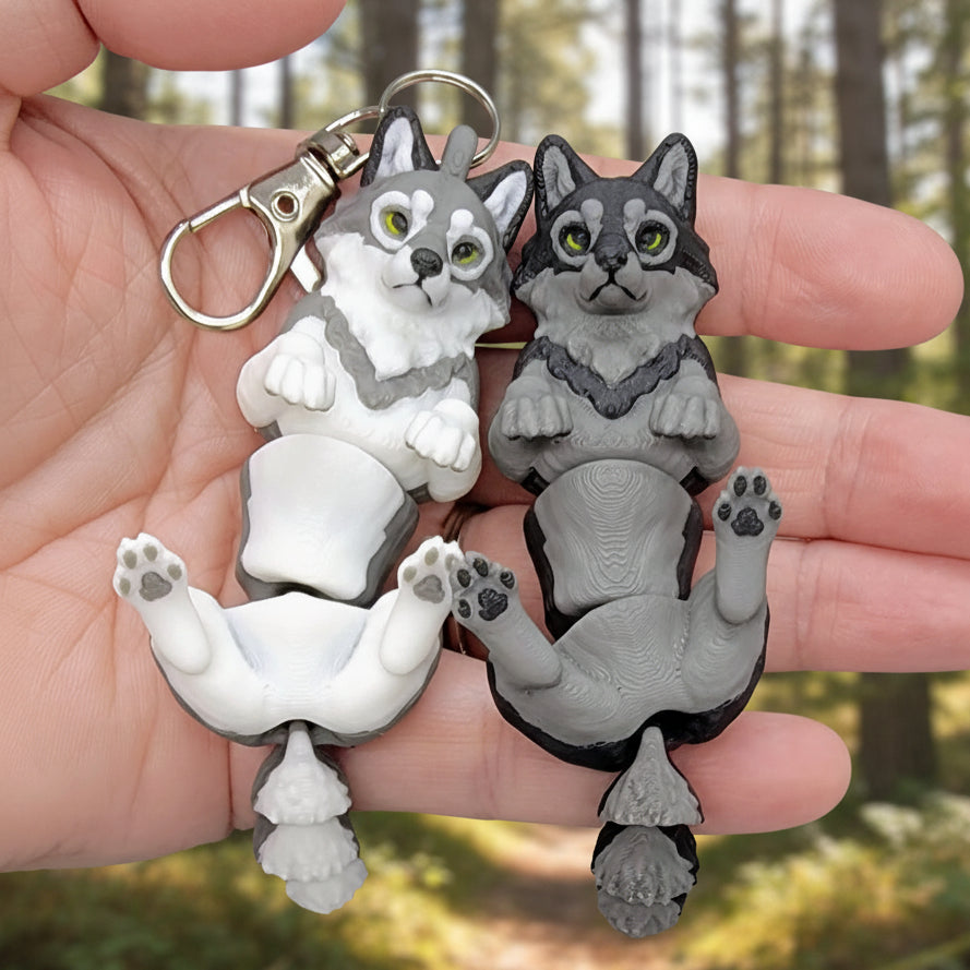 Two articulated wiggle wolf keychains held in hand, one white and one gray, showing playful laying position with visible paw pads and attached keyring, 3D printed fidget toy keychains