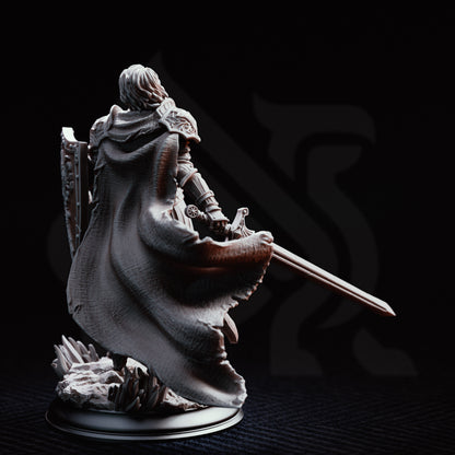 Rear view of the Alwine von Findros resin miniature, showcasing the intricate textures of her tattered, flowing cloak and the detailed engravings on the back of her heavy pauldrons and plate armor. She stands on a rocky scenic base holding her sword and shield.