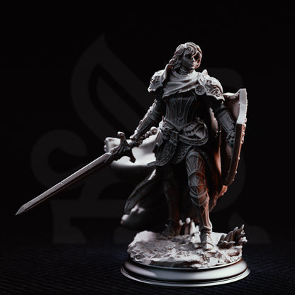 Front view of the Alwine von Findros resin miniature without her helmet, revealing short wavy hair and a focused expression. She is clad in ornate plate armor, holding a longsword and massive shield over a detailed coastal rock terrain base against a black background.