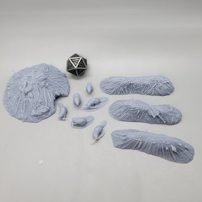 Top-down view of the unpainted resin Beaver Pack scatter set featuring 6 beaver miniatures, 3 dams, 1 lodge, and a D20 die for scale.