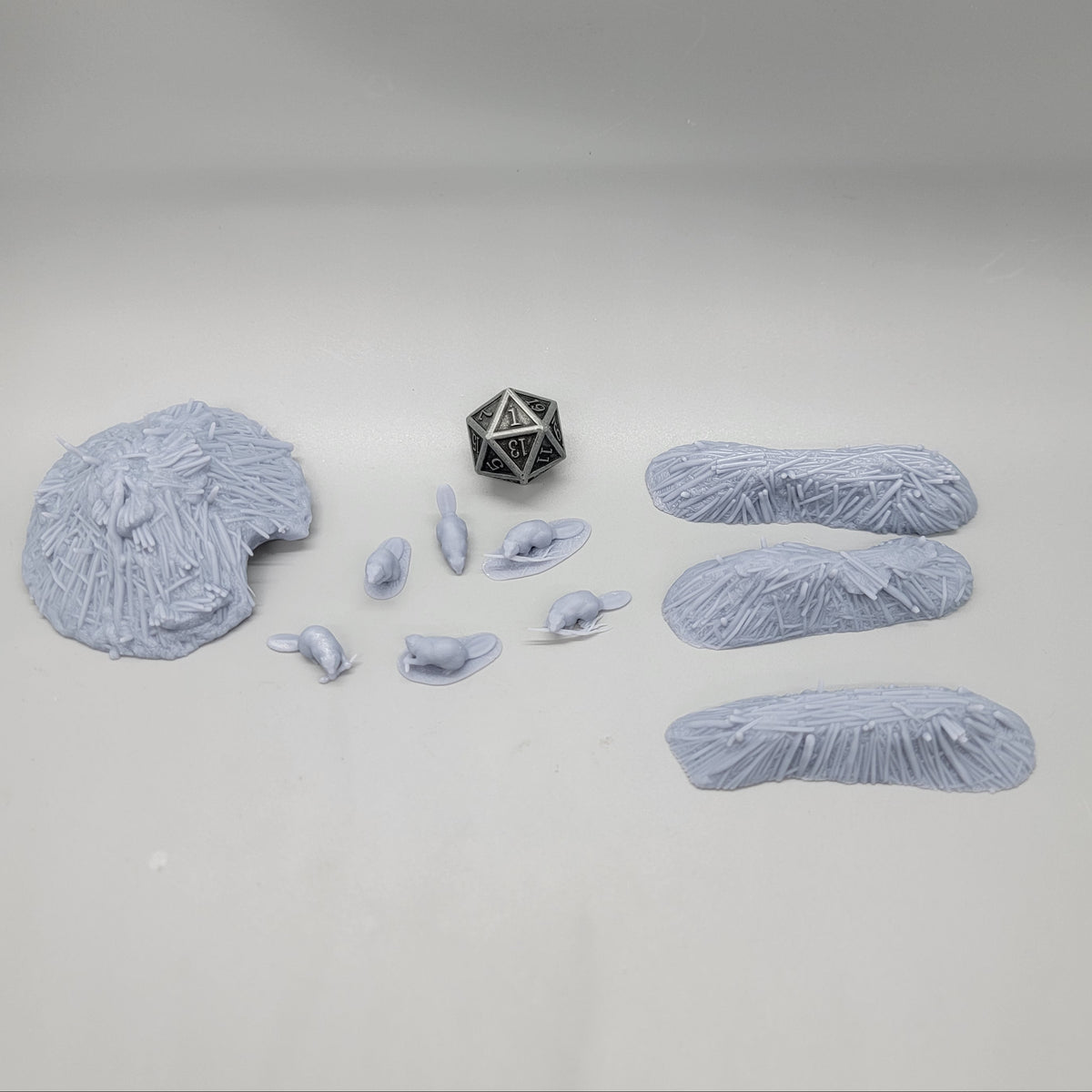 Top-down view of the unpainted resin Beaver Pack scatter set featuring 6 beaver miniatures, 3 dams, 1 lodge, and a D20 die for scale.