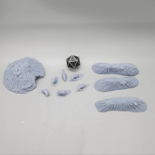 Top-down view of the unpainted resin Beaver Pack scatter set featuring 6 beaver miniatures, 3 dams, 1 lodge, and a D20 die for scale.