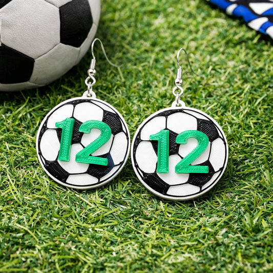 Soccer ball-themed earrings with number 12 on grass with soccer ball in background