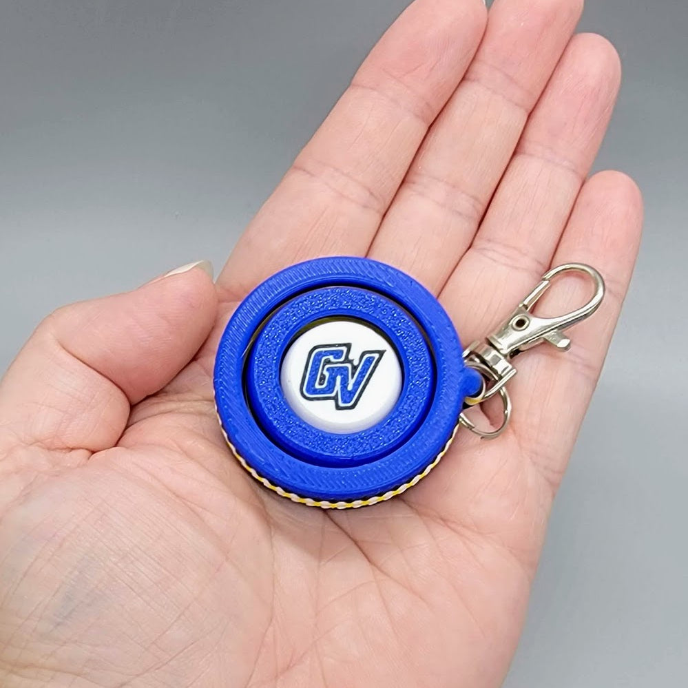 Hand holding the blue and white GV 3D printed fidget spinner keychain to demonstrate scale and size
