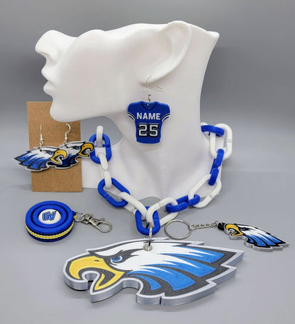Collection of blue and white Grain Valley Eagles spirit accessories including a necklace, jersey earrings, eagle charm, and fidget keychain displayed on a jewelry mannequin.