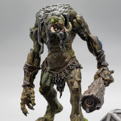Painted Hag Cursed Troll 1 with green-brown skin, pale hair, long tusks, and a wooden club.