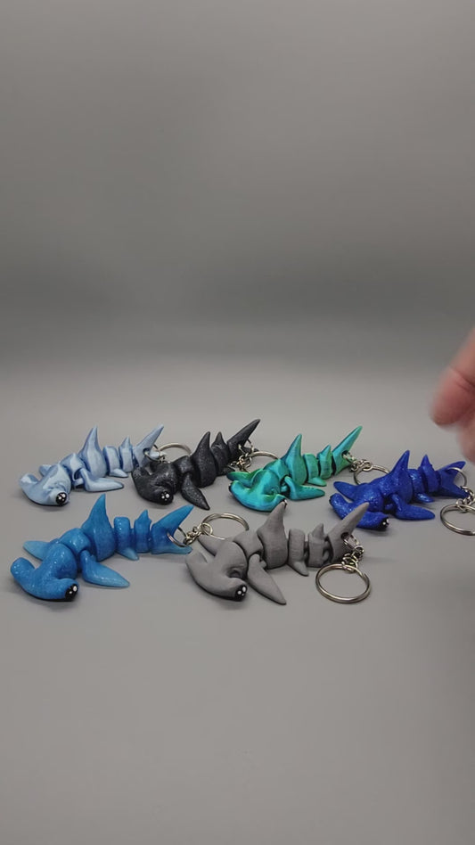 Showcase of miniature hammerhead toys in various blue & grayscale colors with keychains attached.