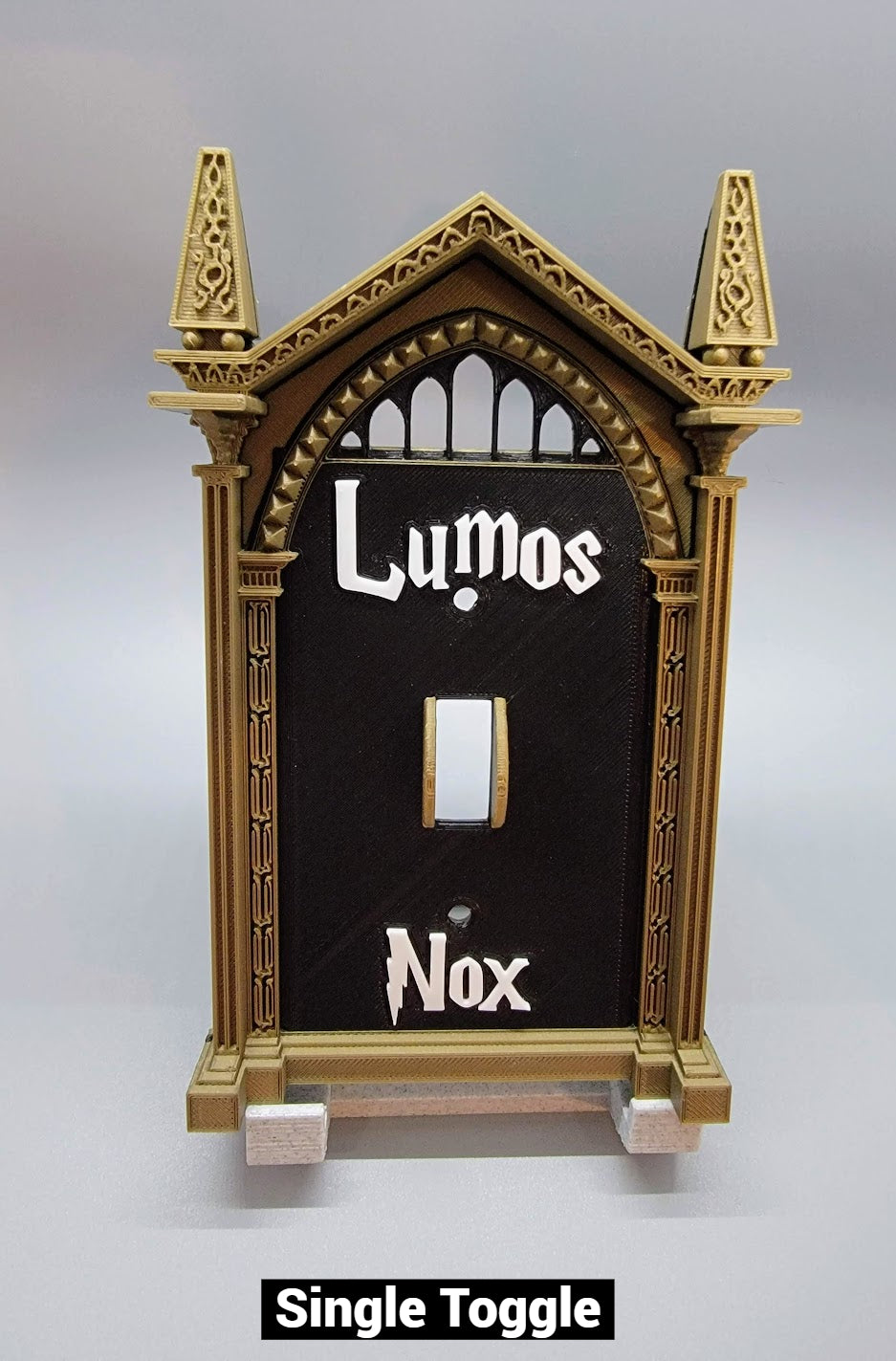 Single toggle wizard light switch cover with custom Lumos and Nox lettering for magical room decor. Shown in Bronze Frame Color, Black Plate Cover, and White Letters
