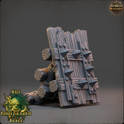 Angled view of the Thumper Board wooden barricade showing reinforced planks, spikes, and log supports.