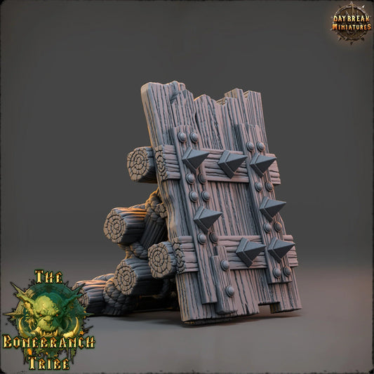 Angled view of the Thumper Board wooden barricade showing reinforced planks, spikes, and log supports.