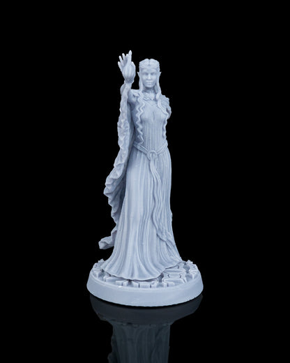 Front view of Valyra the White Lady, an unpainted gray resin elven sorceress miniature with long hair, wearing a braided dress, raising her right hand with a flame effect while standing on a runic stone base.
